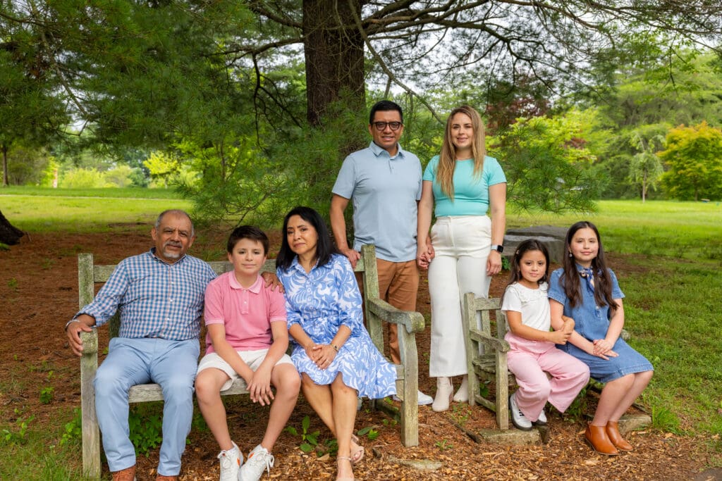 Multi-generational family portrait on a garden bench under tall trees at Meadowlark Botanical Gardens – captured by Capture Joy Photography, Northern Virginia family photographer.