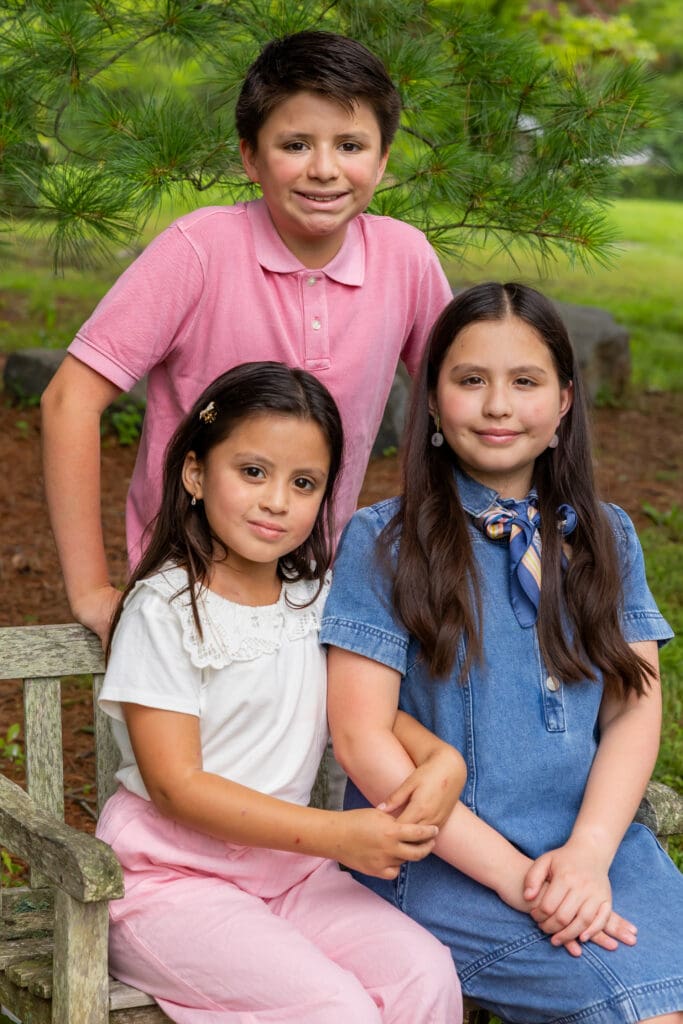 Brother and sisters posing on a wooden bench with trees in the background during a family session – captured by Capture Joy Photography, Northern Virginia family photographer.