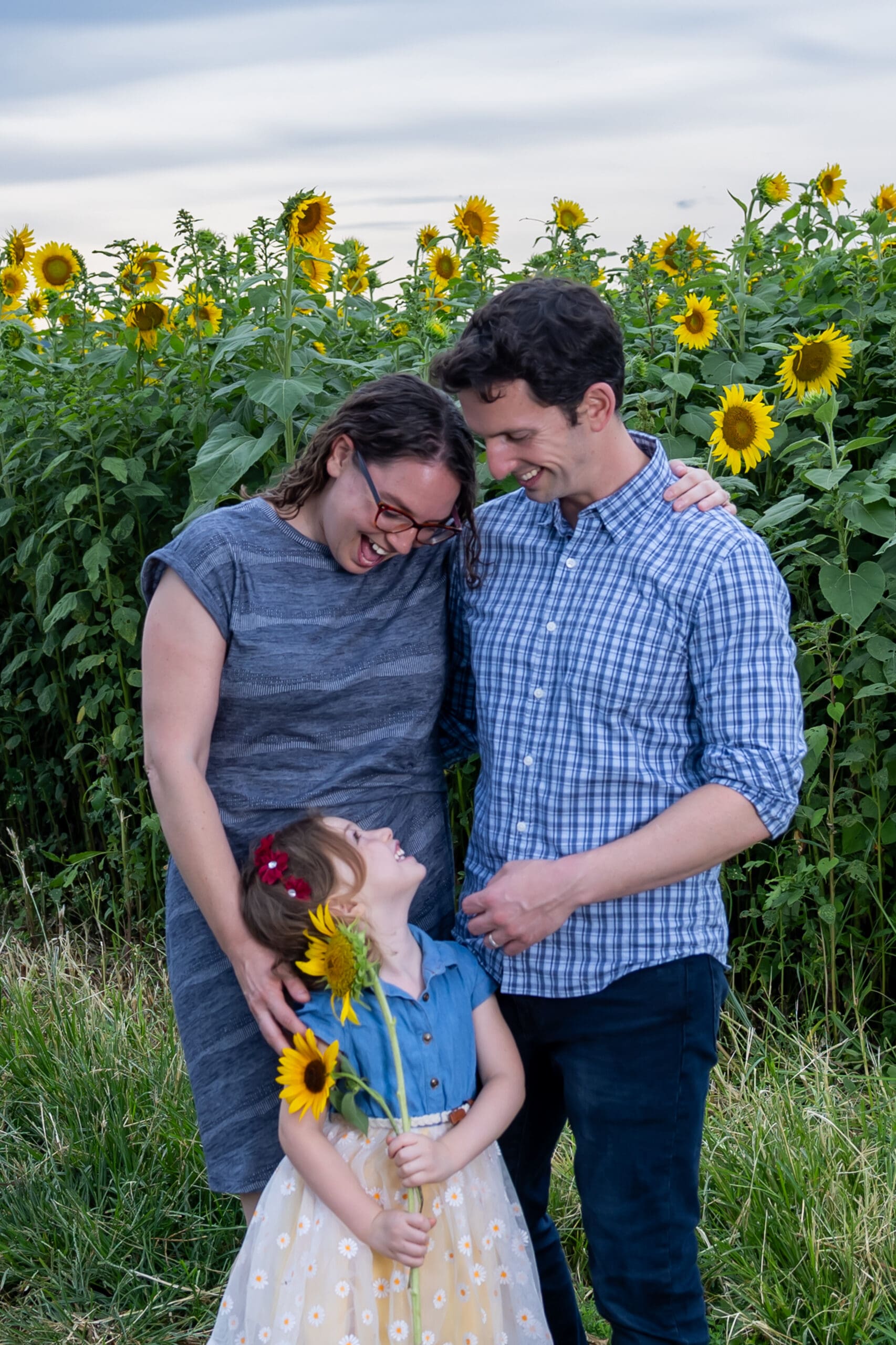 Parents and daughter laughing together in sunflower field, captured by Capture Joy Photography, Northern Virginia family photographer.