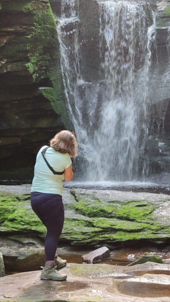 Photographer standing at the base of a waterfall, shooting with Canon R8 and Lemur Strap crossbody camera strap keeping gear secure – captured by Capture Joy Photography, Northern Virginia family photographer.