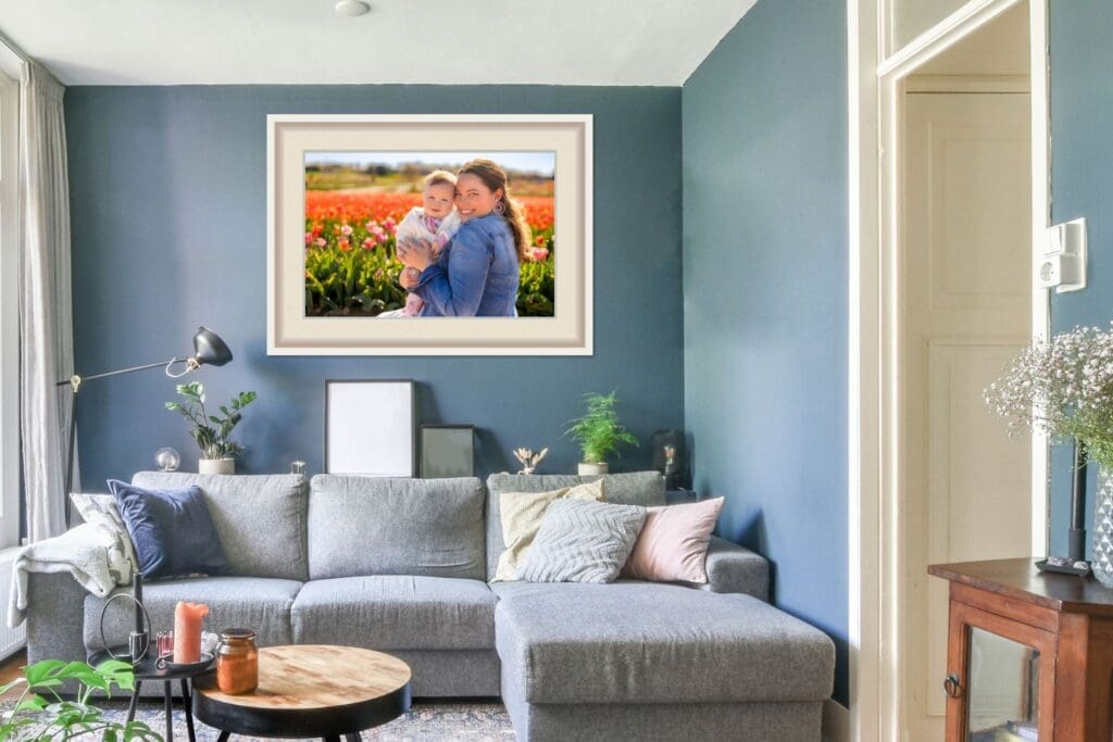 Framed family portrait of mother and baby in tulip field displayed above a grey sectional in a modern living room, showing how heirloom wall art adds warmth and personality to home decor, captured by Capture Joy, Northern Virginia family photographer.