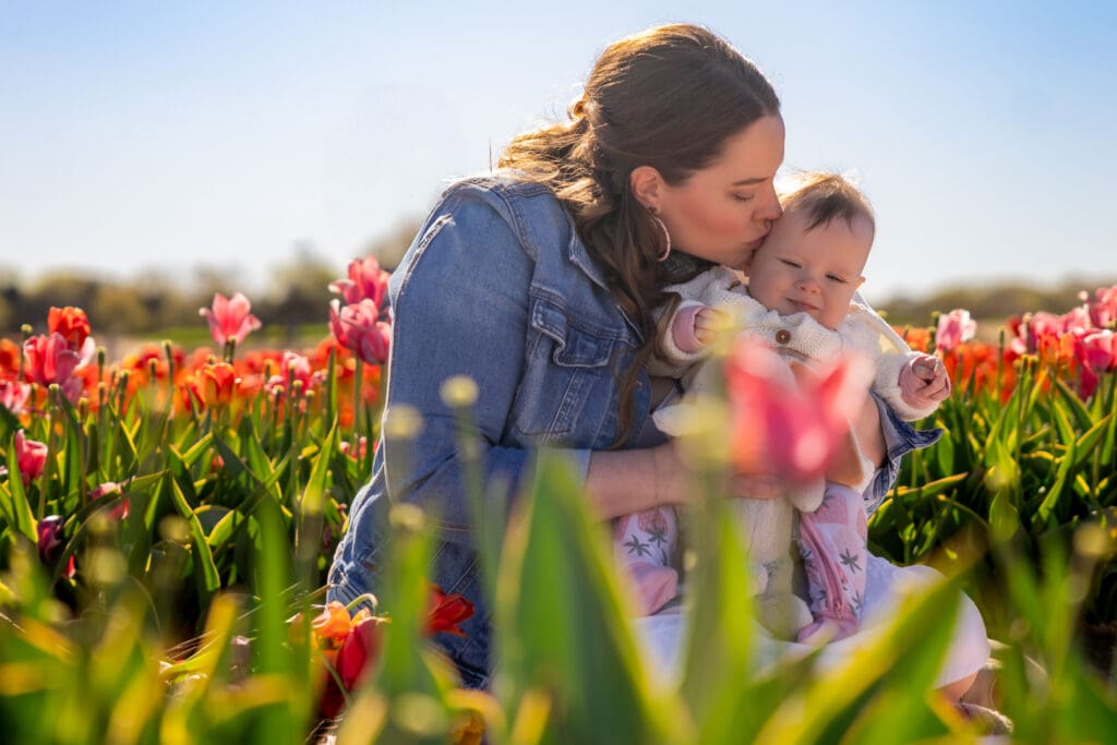 Tender mother and baby moment, partially hidden by pink tulips in bloom – captured by Capture Joy Photography, Northern Virginia family photographer.