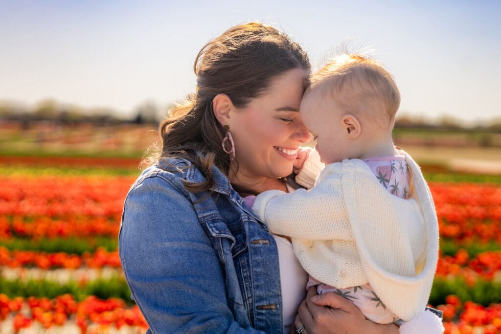 lovingly looking down at baby girl in a field of tulips during golden hour – captured by Capture Joy Photography, Northern Virginia family photographer.